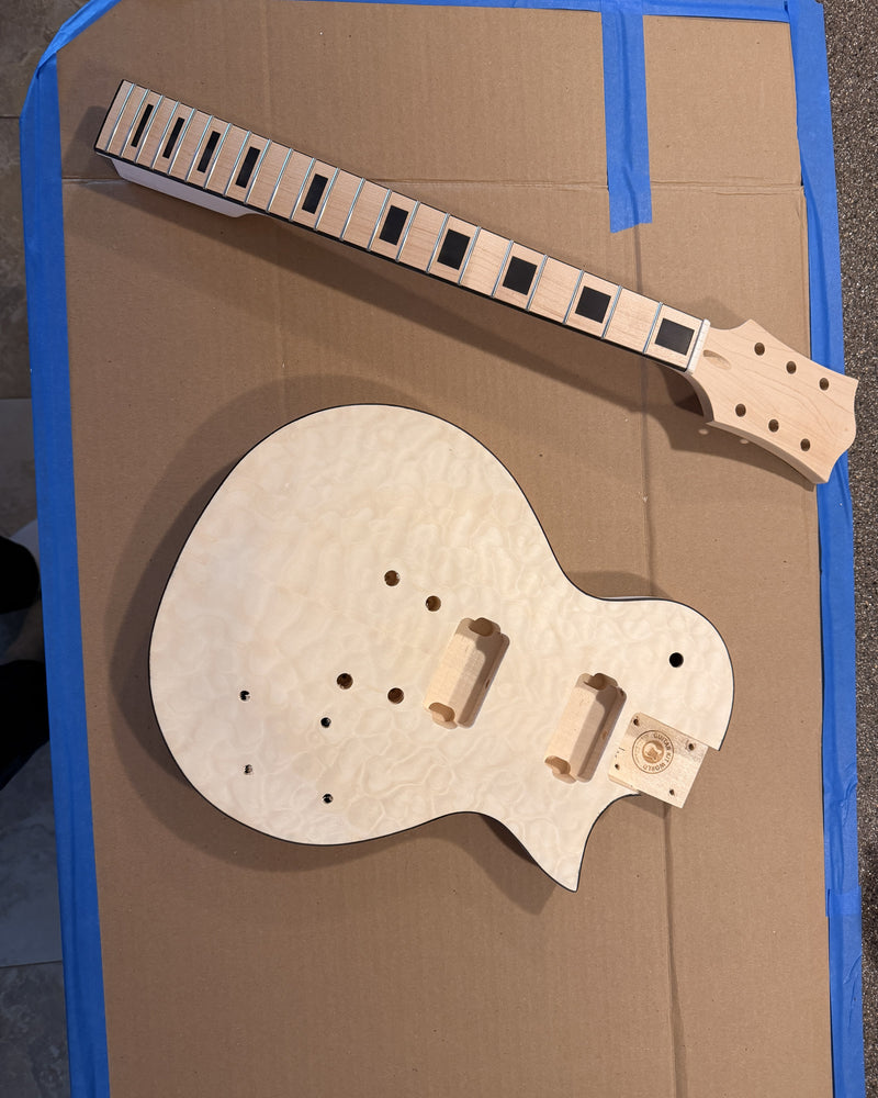 An unassembled guitar kit as it arrives: quilted maple top body and a maple neck with block inlays