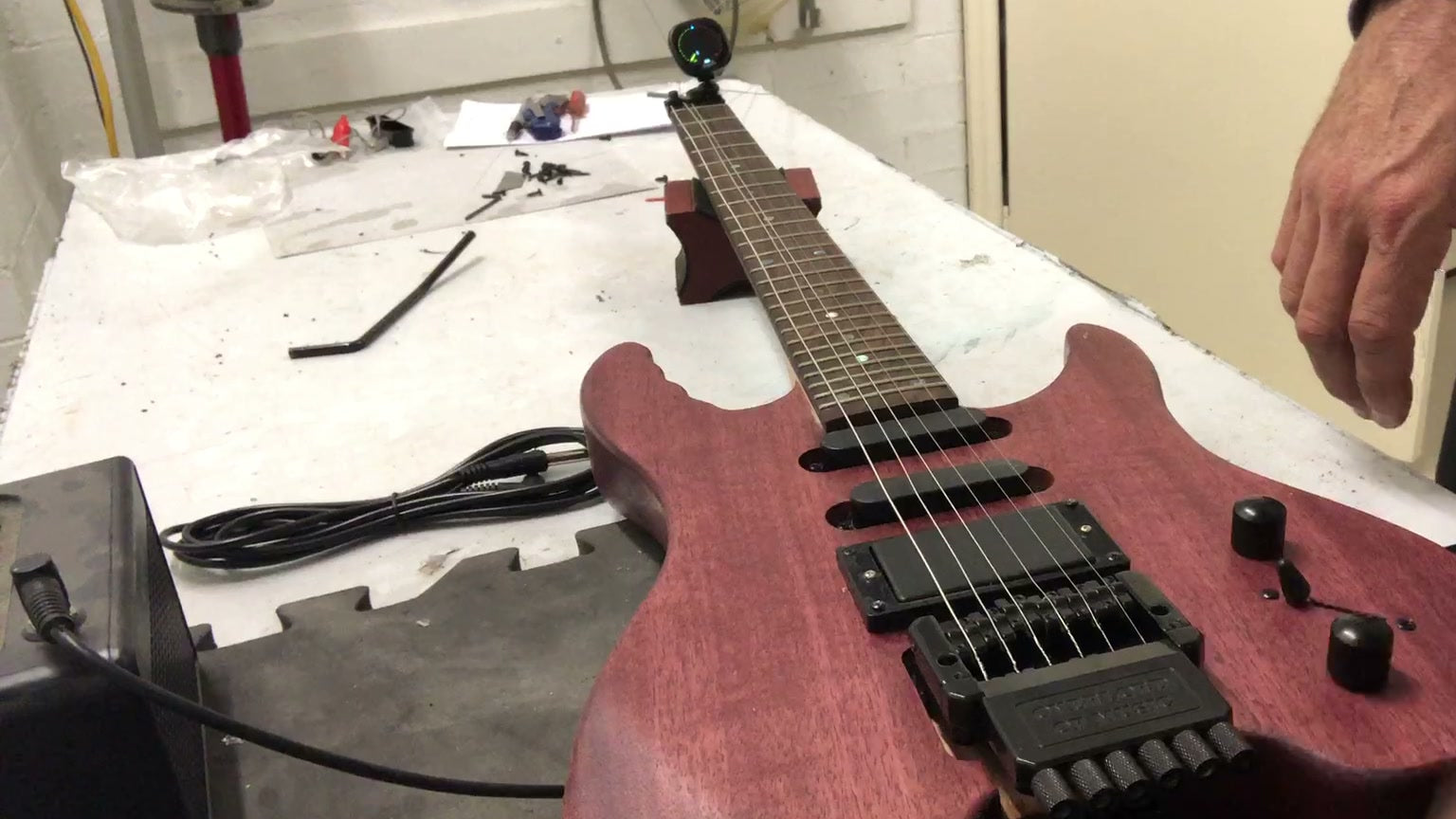 Assembled headless electric guitar kit on a workbench, the neck ending in a string clamp where a headstock would be, with the tuners built into the bridge