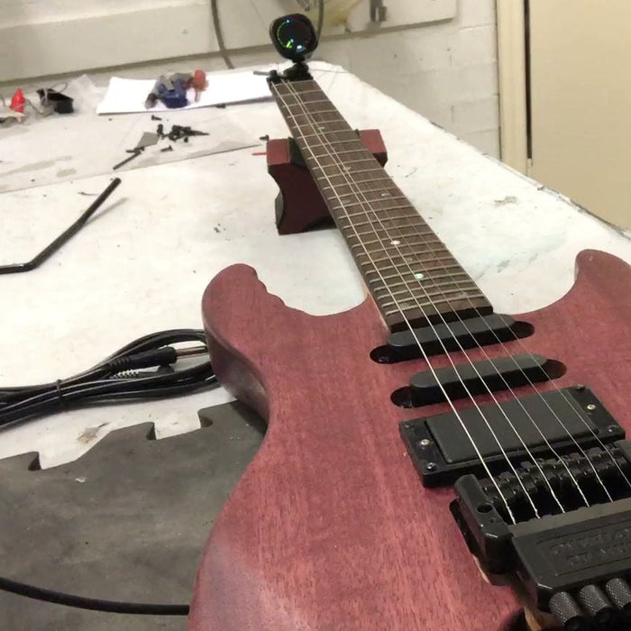 Assembled headless electric guitar kit on a workbench, the neck ending in a string clamp where a headstock would be, with the tuners built into the bridge
