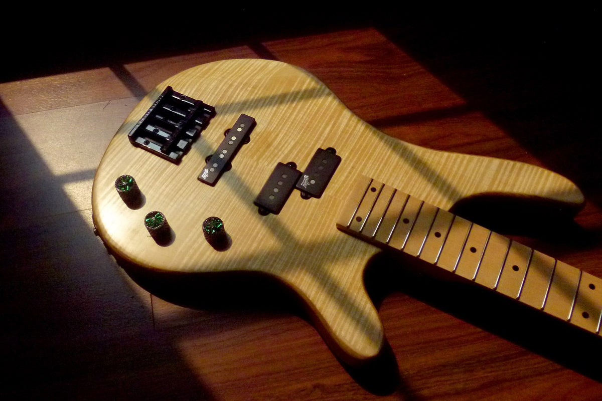 Finished natural oil bass leaning in low afternoon light, flamed maple top with black hardware and maple fretboard