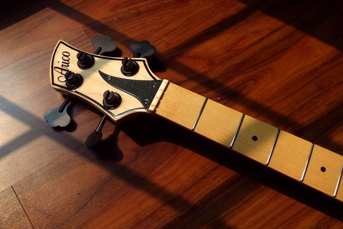 Bass headstock with a script Arico logo, black ultralight tuners with clover-shaped keys, and a bone nut