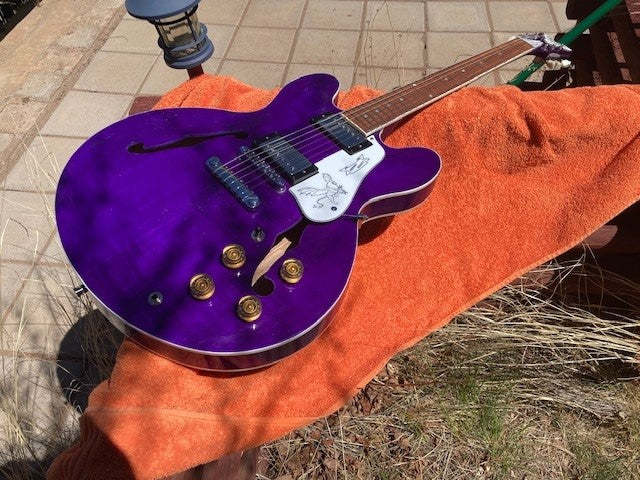 Natural wood offset guitar with a black pickguard and a hand-drawn bird graphic on the body
