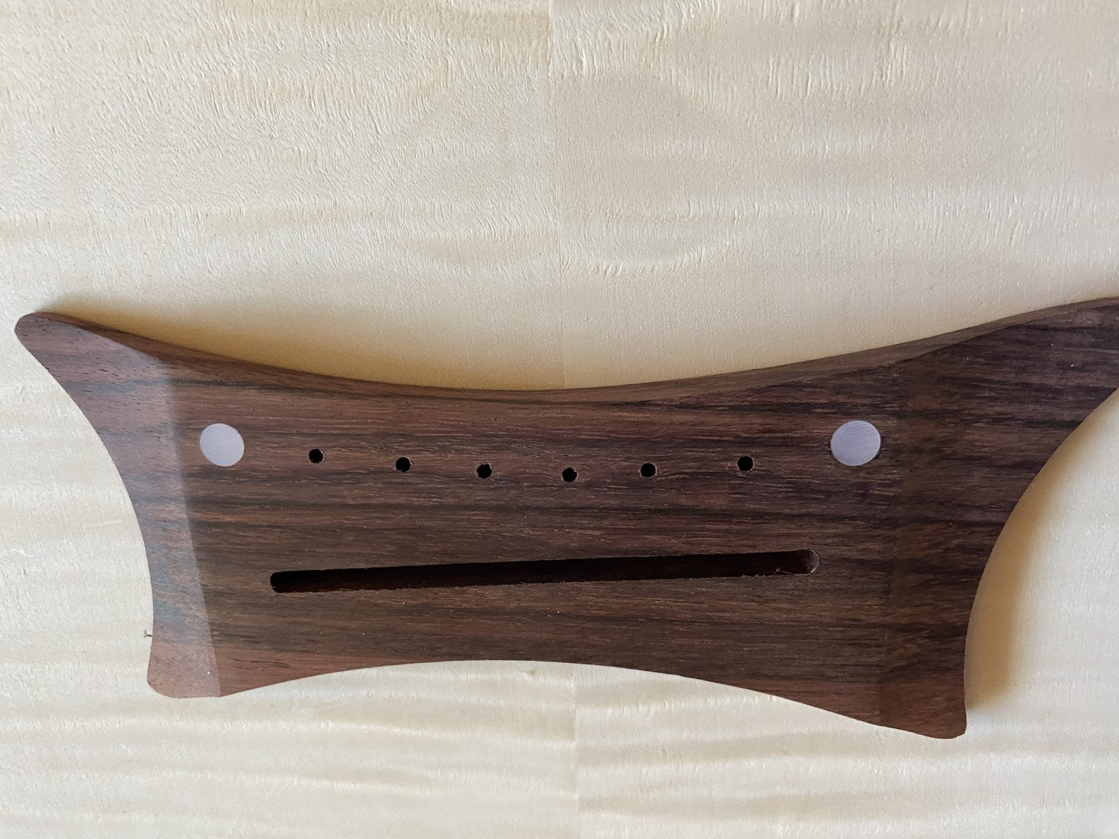 An acoustic-style bridge before gluing, with the saddle slot cut and six bridge pin holes drilled through it