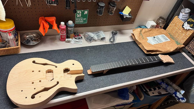 Unfinished semi-hollow baritone guitar kit body and neck laid out on a workshop bench