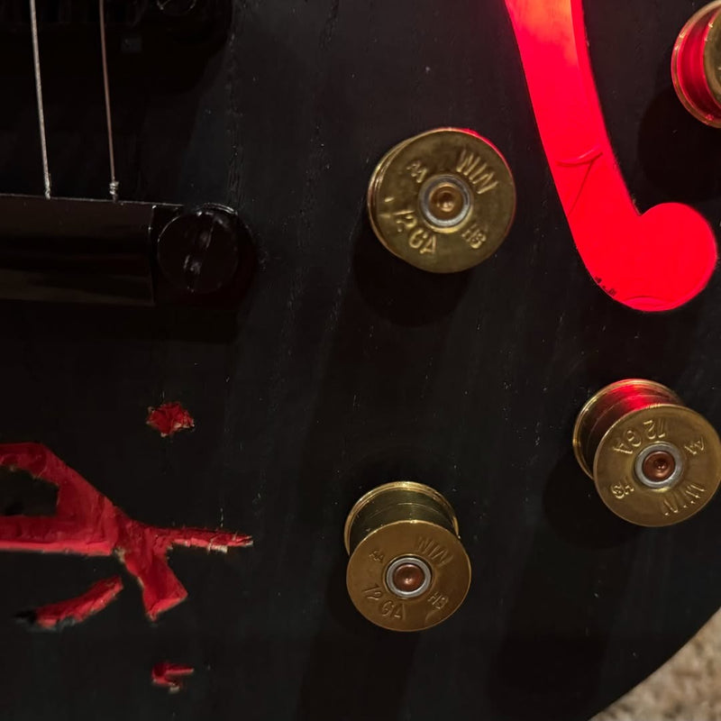 Three spent brass shotgun shells fitted as control knobs on a dark green guitar body