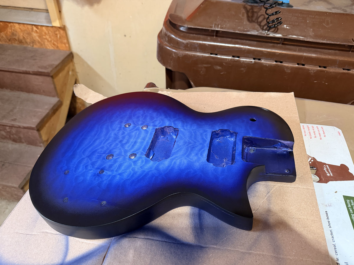 Blue burst guitar body in matte finish on brown paper in a workshop before clear coat