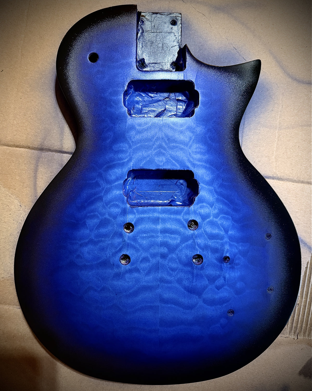 Guitar body with blue burst sprayed, dark edges fading to bright blue center, cavities still masked
