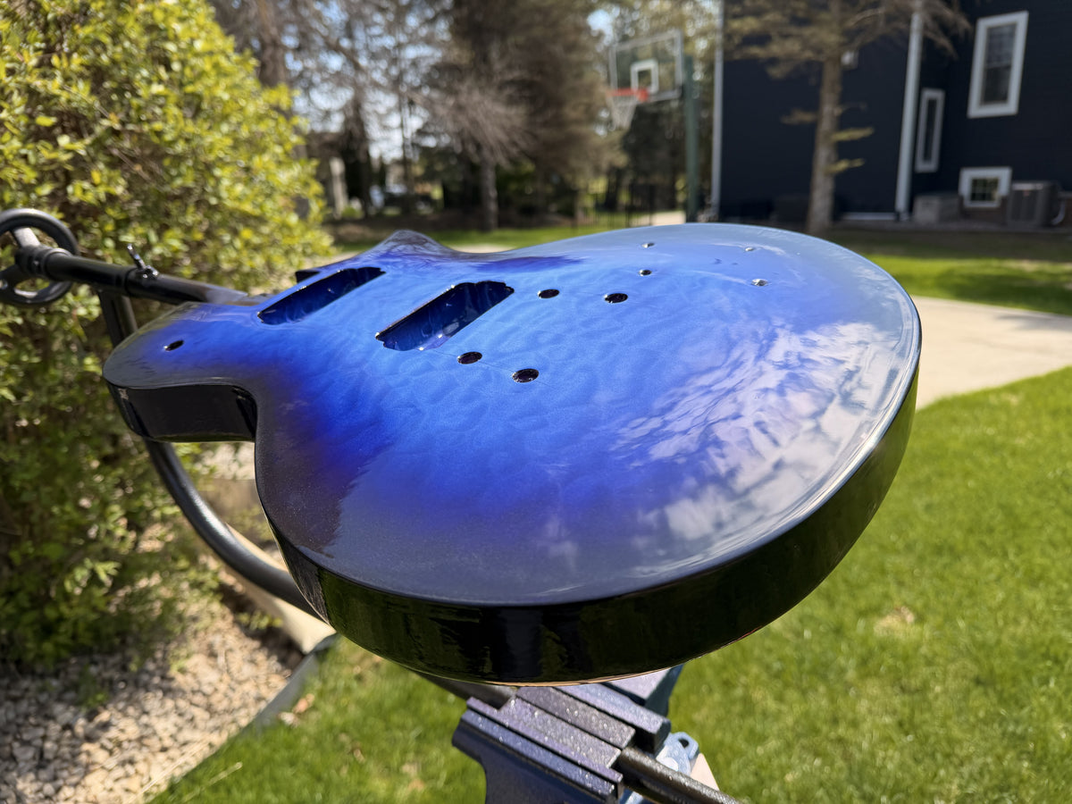 Glossy blue burst guitar body with quilted maple figure visible, photographed outdoors in daylight