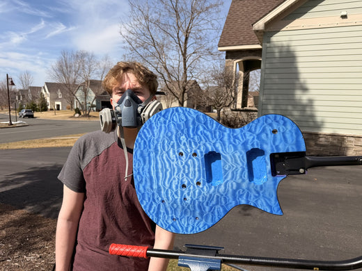 Builder in a half face respirator holding the blue dyed quilted maple body outdoors