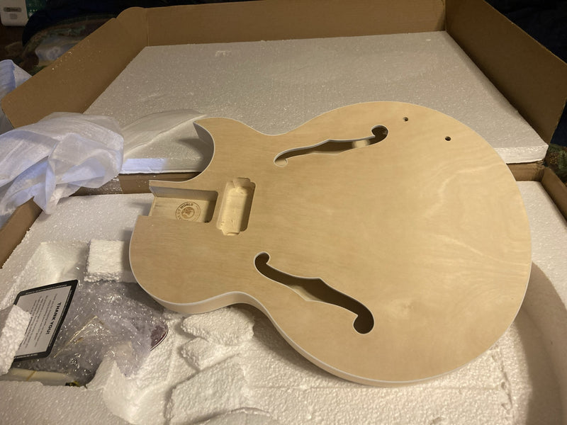 Unfinished natural maple archtop body with f-holes, resting in its foam packing