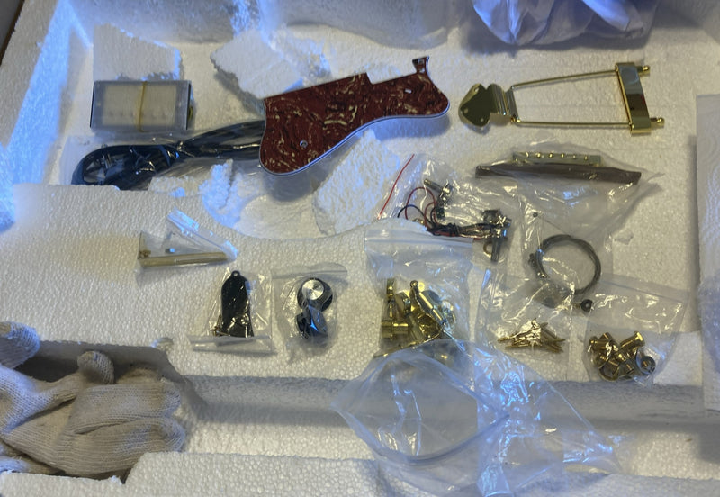 Gold guitar kit hardware laid out: trapeze tailpiece, tortoiseshell pickguard, tuners and pots