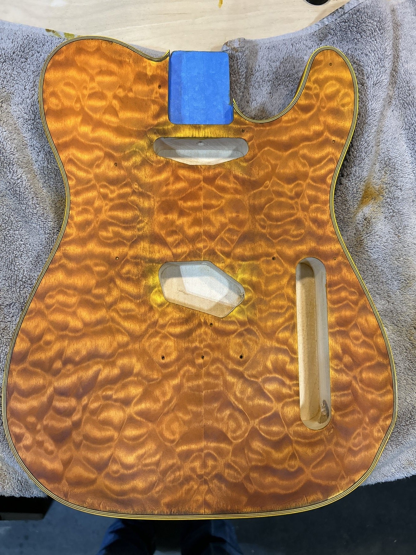 Amber quilted maple T-style guitar body during the build, routed for pickups