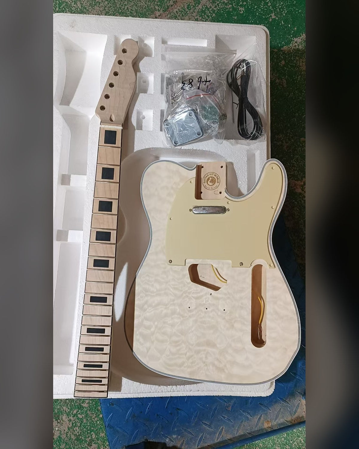 Unfinished single-cutaway guitar kit, quilted maple top, white binding, maple neck with black block inlays, in foam packing