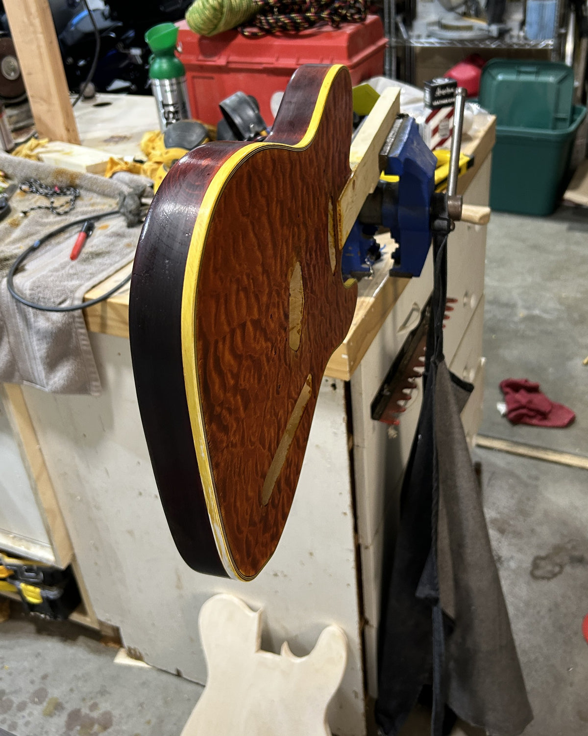 Side of a dyed quilted maple guitar body showing the binding stained yellow by dye and oil before scraping