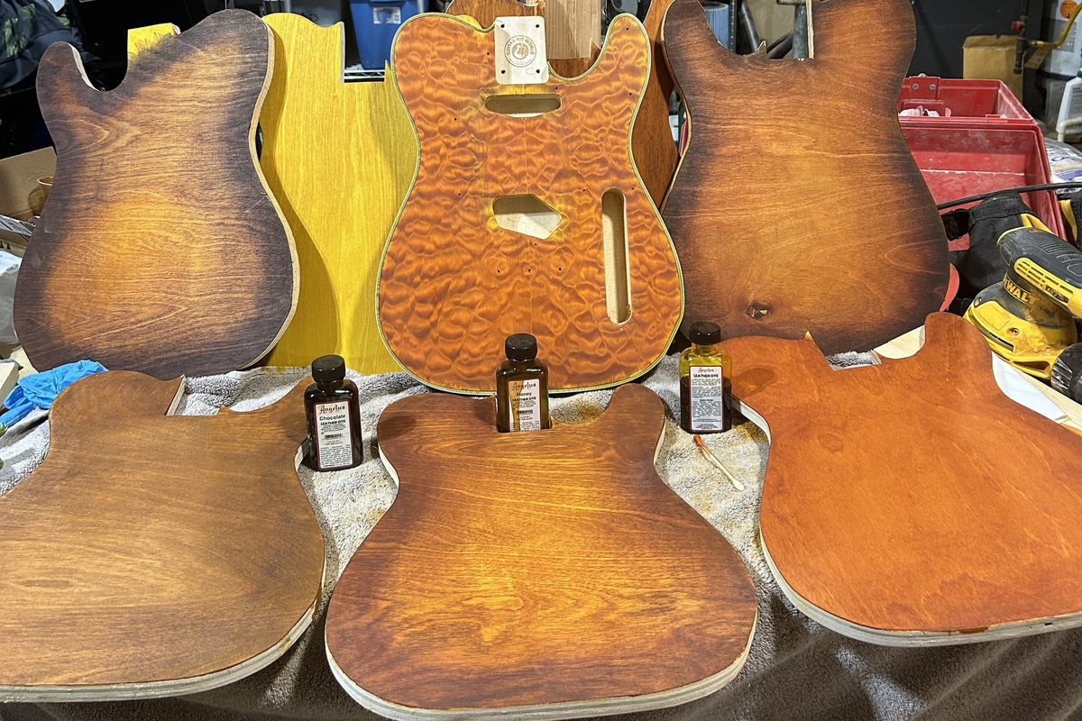 Maple plywood test blanks in sunburst and amber dye around a dyed quilted maple guitar body, leather dye bottles in front