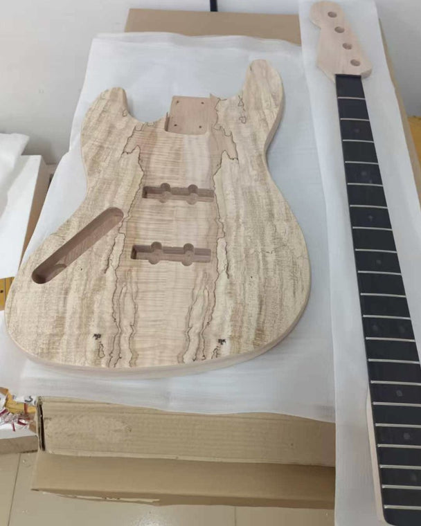 Unfinished bass guitar kit body with a spalted maple veneer top, next to its neck, in the shipping packaging