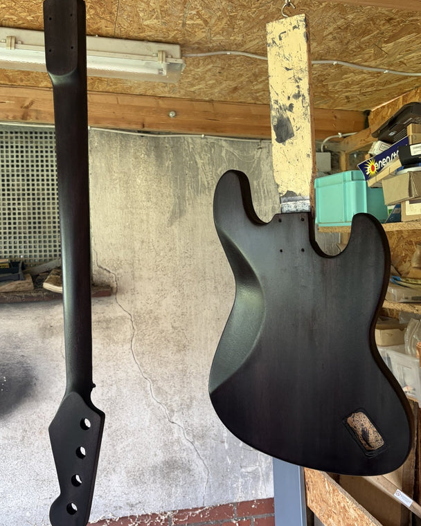Bass neck and body both stained black, hanging side by side to dry in a home workshop