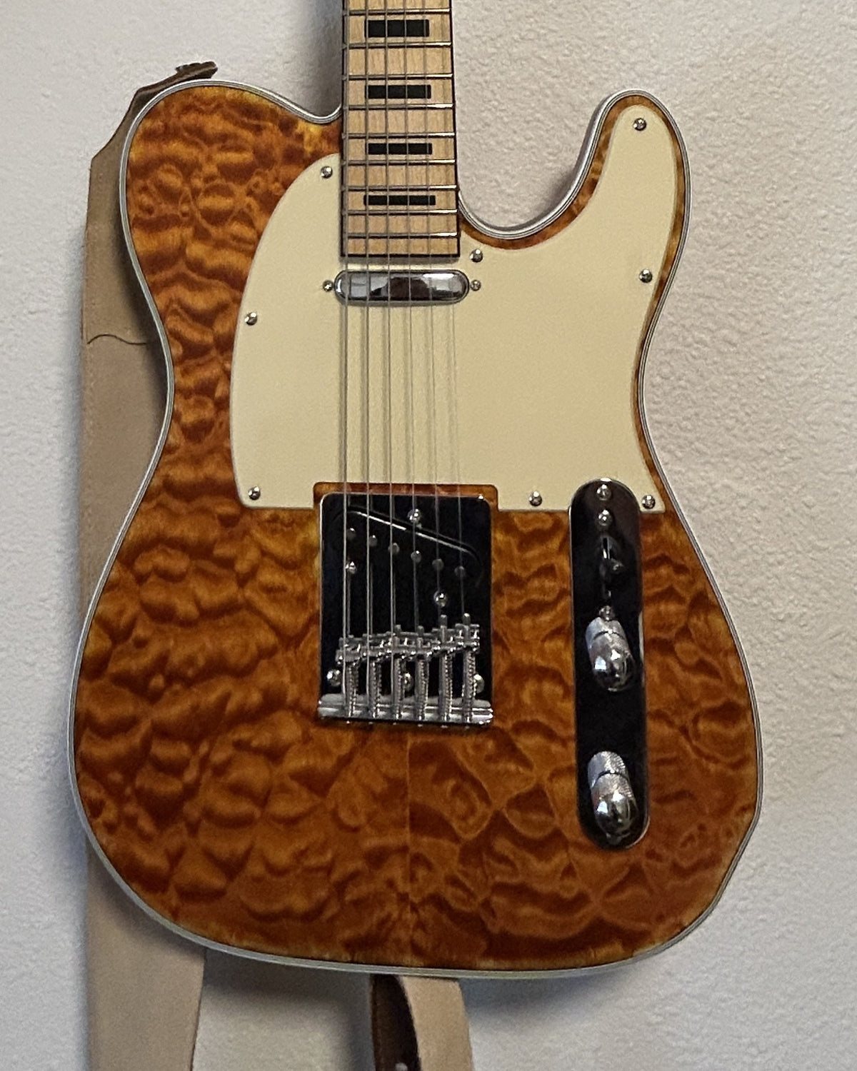Close-up of the finished quilted maple top under Tru-Oil and paste wax, with the cream pickguard and chrome control plate
