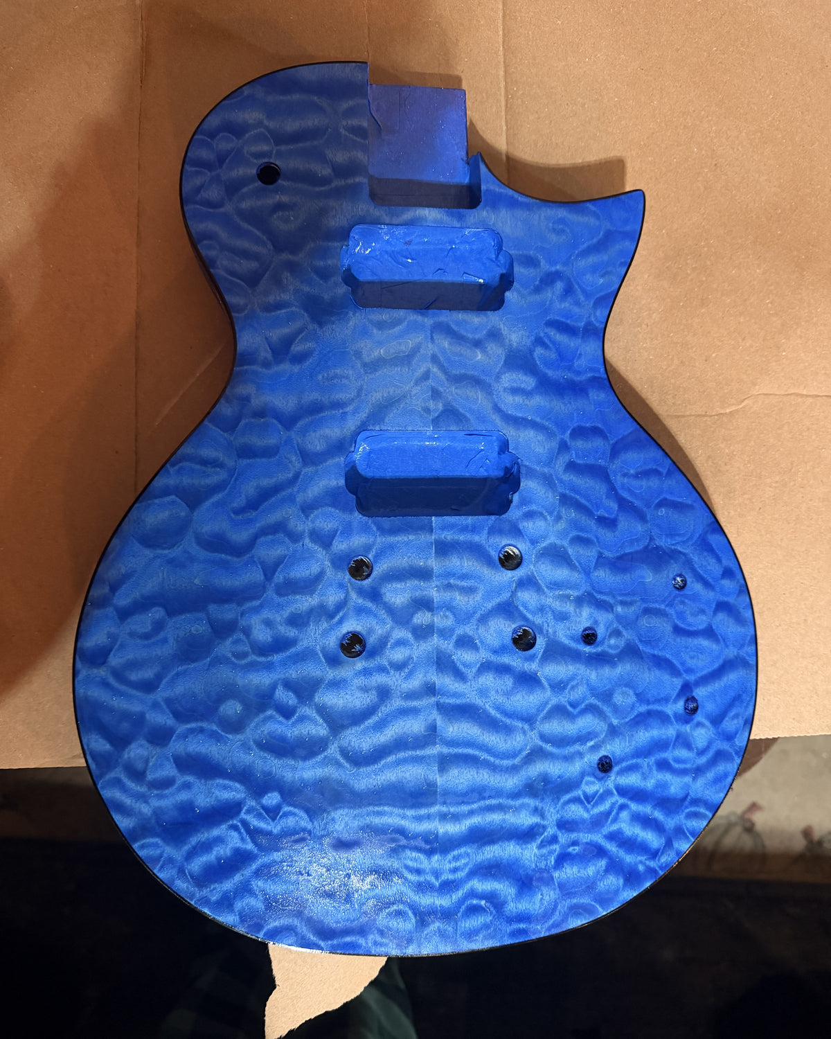Guitar body top dyed bright blue, quilted maple figure showing strongly, pickup cavities masked with tape