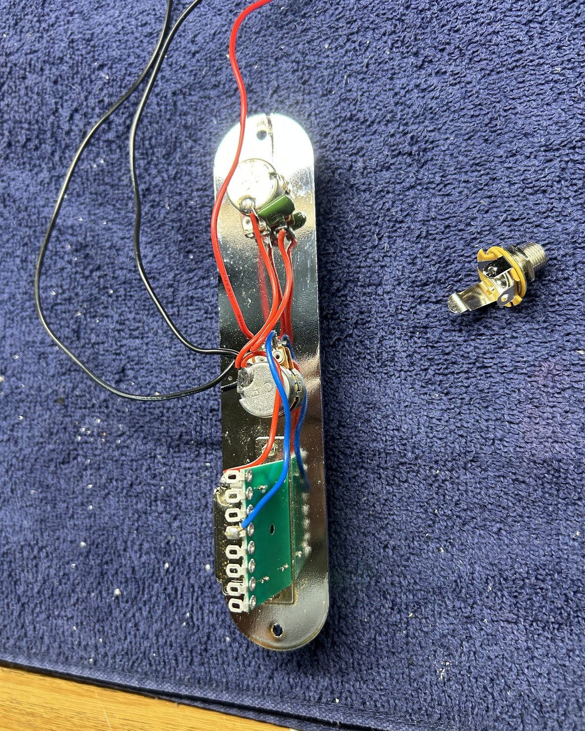Chrome guitar control plate with volume and tone pots and a 3-way switch, half soldered, output jack beside it