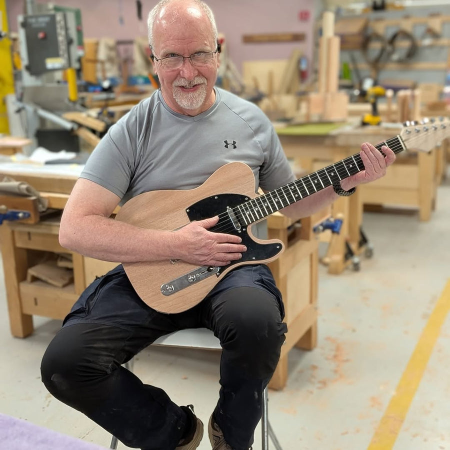 Builder seated with the electric guitar they completed at the Fairfax guitar building workshop